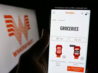 Stuttgart, Almanya - 12-31-2023: Logo önünde ABD 'li fast food şirketi Whataburger Restaurants LLC' nin web sayfası ile cep telefonu tutan kişi. Telefon ekranının merkezine odaklan.