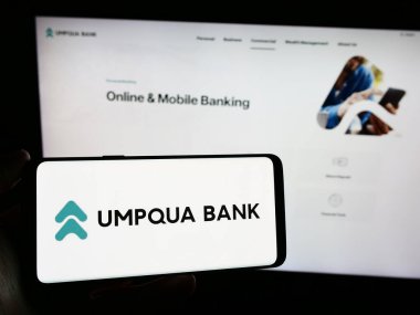 Stuttgart, Almanya - 02-03-2024: Amerikan finans hizmetleri şirketi Umpqua Bank 'ın logosunun bulunduğu cep telefonu sahibi kişi iş sayfasının önünde. Telefon ekranına odaklan.