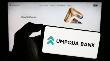 Stuttgart, Almanya - 02-03-2024: ABD 'li finans hizmetleri şirketi Umpqua Bank' ın logosunun bulunduğu akıllı telefon sahibi kişi web sitesi önünde. Telefon ekranına odaklan.
