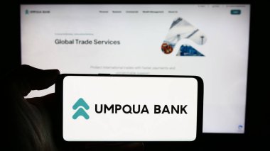 Stuttgart, Almanya - 02-03-2024: ABD 'li finans hizmetleri şirketi Umpqua Bank' ın logosuyla cep telefonu sahibi kişi iş sayfası önünde. Telefon ekranına odaklan.