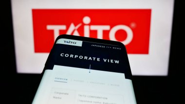 Stuttgart, Almanya - 02-03-2024: Japon video oyunları şirketi Taito Corporation 'ın internet sitesi ile birlikte iş logosu önünde akıllı telefon. Telefon ekranının sol üst kısmına odaklan.