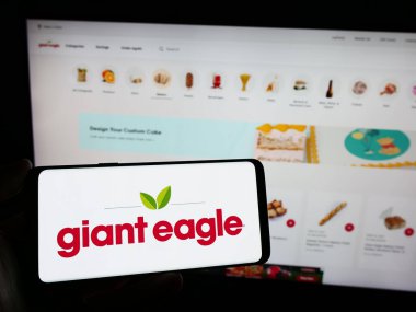 Stuttgart, Almanya - 02-03-2024: Üzerinde ABD 'li süpermarket zincir şirketi Giant Eagle Inc.' in logosu olan cep telefonu sahibi kişi iş sayfasının önünde. Telefon ekranına odaklan.