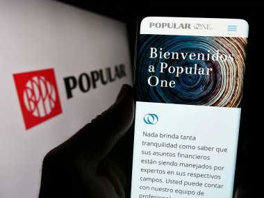Stuttgart, Almanya - 02-06-2024: Finans hizmetleri şirketi Banco Popular de Puerto Rico 'nun logolu web sayfası ile cep telefonu tutan kişi. Telefon ekranının merkezine odaklan.
