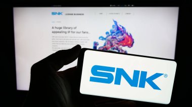 Stuttgart, Germany - 02-06-2024: Person holding smartphone with logo of Japanese video games company SNK Corporation in front of website. Focus on phone display. clipart