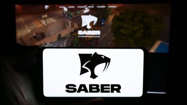 Stuttgart, Almanya - 02-06-2024: Web sayfası önünde Saber Interactive Inc. şirketinin logosu olan cep telefonu sahibi kişi. Telefon ekranına odaklan.