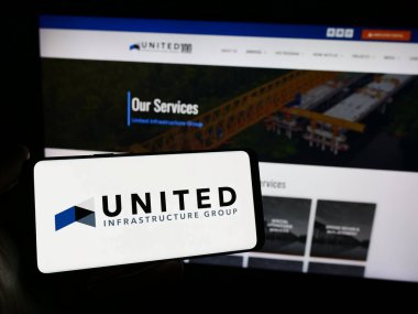 Stuttgart, Germany - 02-07-2023: Person holding smartphone with logo of US investment company United Infrastructure Group in front of website. Focus on phone display. clipart