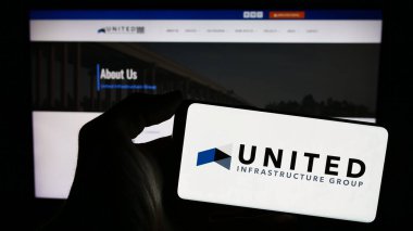 Stuttgart, Almanya - 02-07-2023: Amerikan yatırım şirketi United Infrastructure Group 'un logosunu web sayfasının önünde tutan kişi. Telefon ekranına odaklan.