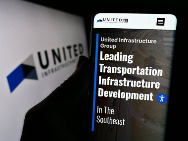 Stuttgart, Almanya - 02-07-2023: ABD 'li yatırım şirketi United Infrastructure Group' un web sayfası ile logo önünde cep telefonu tutan kişi. Telefon ekranının merkezine odaklan.