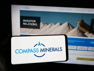 Stuttgart, Almanya - 02-08-2024: ABD 'li maden şirketi Compass Minerals International Inc.' in logosuyla cep telefonu sahibi kişi iş sayfasının önünde. Telefon ekranına odaklan.