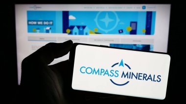 Stuttgart, Almanya - 02-08-2024: İnternet sayfası önünde üzerinde Amerikan maden şirketi Compass Minerals International Inc. 'in logosu bulunan cep telefonu sahibi kişi. Telefon ekranına odaklan.