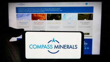 Stuttgart, Almanya - 02-08-2024: İnternet sitesi önünde üzerinde ABD 'li maden şirketi Compass Minerals International Inc.' in logosu bulunan akıllı telefon sahibi kişi. Telefon ekranına odaklan.