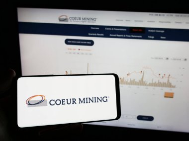 Stuttgart, Almanya - 02-08-2024: Üzerinde Amerikan değerli metal şirketi Coeur Mining Inc. 'in logosu bulunan cep telefonu sahibi kişi iş sayfasının önünde. Telefon ekranına odaklan.