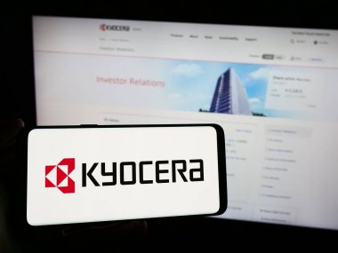 Stuttgart, Almanya - 02-08-2024: Japon elektronik şirketi Kyocera Corporation 'ın logosunun bulunduğu cep telefonu sahibi kişi iş sayfasının önünde. Telefon ekranına odaklan.