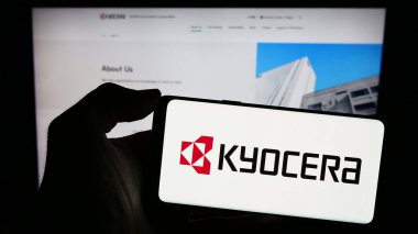 Stuttgart, Almanya - 02-08-2024: Japon elektronik şirketi Kyocera Corporation 'ın logosuyla cep telefonu sahibi kişi iş sayfasının önünde. Telefon ekranına odaklan.