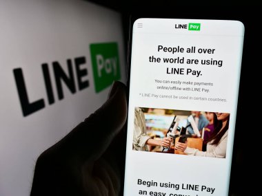 Stuttgart, Germany - 02-11-2024: Person holding cellphone with webpage of Thai payments company LINE Pay in front of business logo. Focus on center of phone display. clipart