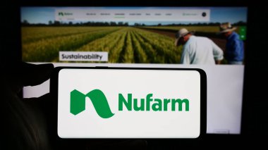 Stuttgart, Almanya - 02-12-2024: Avustralyalı tarım kimya şirketi Nufarm Limited 'in logosunun bulunduğu cep telefonu sahibi kişi iş sayfasının önünde. Telefon ekranına odaklan.