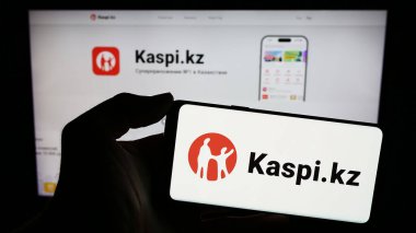 Stuttgart, Almanya - 02-13-2024: İş sayfası önünde Kazak finans hizmetleri şirketi Kaspi.kz 'in logosuyla cep telefonu tutan kişi. Telefon ekranına odaklan.