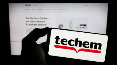 Stuttgart, Almanya - 02-13-2024: Alman enerji hizmetleri şirketi Techem GmbH 'nin logosunu taşıyan cep telefonu sahibi kişi iş sayfasının önünde. Telefon ekranına odaklan.
