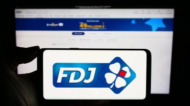 Stuttgart, Almanya - 02-13-2024: Fransız piyango şirketi Francaise des Jeux 'un (FDJ) logosuyla cep telefonu tutan kişi iş sayfasının önünde. Telefon ekranına odaklan.