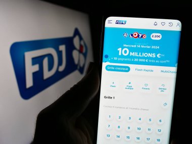 Stuttgart, Almanya - 02-13-2024: Logo önünde Fransız piyango şirketi Francaise des Jeux 'un (FDJ) web sayfası ile cep telefonu tutan kişi. Telefon ekranının merkezine odaklan.