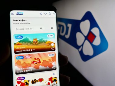 Stuttgart, Almanya - 02-13-2024: Logo önünde Fransız piyango şirketi Francaise des Jeux 'un (FDJ) web sayfası ile cep telefonu tutan kişi. Telefon ekranının merkezine odaklan.