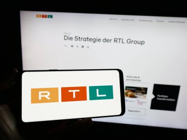 Stuttgart, Almanya - 02-13-2024: İçinde medya ve televizyon şirketi RTL Group S.A. 'nın logosu bulunan cep telefonu sahibi kişi iş sayfası önünde. Telefon ekranına odaklan.