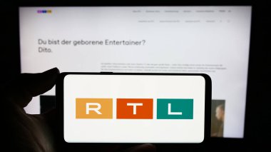 Stuttgart, Almanya - 02-13-2024: Medya ve televizyon şirketi RTL Group S.A. 'nın logosuna sahip cep telefonu sahibi kişi iş sayfası önünde. Telefon ekranına odaklan.