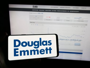 Stuttgart, Almanya - 02-14-2024: Amerikan emlak şirketi Douglas Emmett Inc. 'in logosuna sahip cep telefonu sahibi kişi iş sayfasının önünde. Telefon ekranına odaklan.