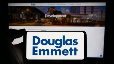 Stuttgart, Almanya - 02-14-2024: ABD 'li emlak şirketi Douglas Emmett Inc.' in logosuyla cep telefonu sahibi kişi iş sayfasının önünde. Telefon ekranına odaklan.