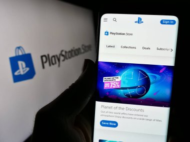 Stuttgart, Almanya - 02-14-2024: Oyun çevrimiçi mağazası PlayStation Store (PS Store) web sitesinin logosu önünde cep telefonu tutan kişi. Telefon ekranının merkezine odaklan.