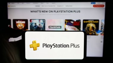 Stuttgart, Almanya - 02-14-2024: İş sayfası önünde abonelik servisi PlayStation Plus (PS Plus) logosu olan cep telefonu sahibi kişi. Telefon ekranına odaklan.