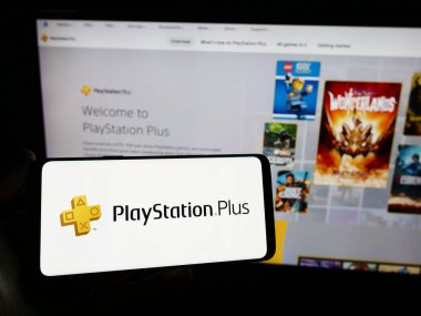 Stuttgart, Almanya - 02-14-2024: İnternet sitesinin önünde abonelik servisi PlayStation Plus (PS Plus) logosu olan akıllı telefon sahibi kişi. Telefon ekranına odaklan.