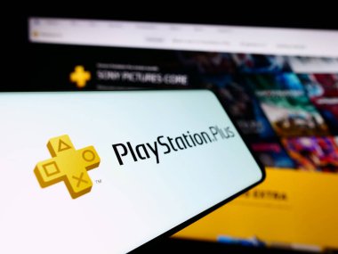 Stuttgart, Almanya - 02-14-2024: İş sitesinin önünde abonelik servisi PlayStation Plus (PS Plus) logosu bulunan cep telefonu. Telefon ekranının soluna odaklan.