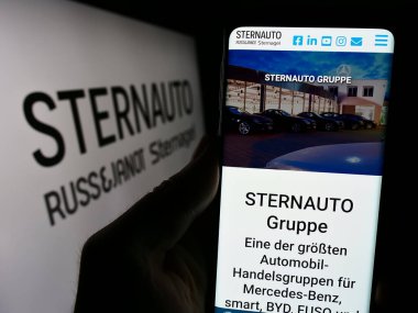 Stuttgart, Almanya - 02-15-2024: Alman otomobil dağıtım şirketi Stern Auto Holding GmbH 'nin web sitesiyle logo önünde cep telefonu tutan kişi. Telefon ekranının merkezine odaklan.