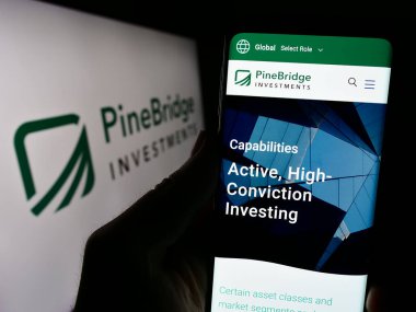 Stuttgart, Almanya - 02-15-2024: Logo önünde ABD 'li yatırım şirketi PineBridge Investments LLC' nin web sitesiyle cep telefonu bulunduran kişi. Telefon ekranının merkezine odaklan.