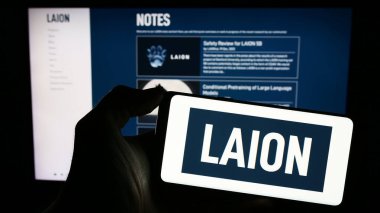 Stuttgart, Germany - 02-15-2024: Person holding cellphone with logo of Large-scale Artificial Intelligence Open Network (LAION) in front of webpage. Focus on phone display. clipart