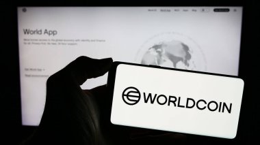 Stuttgart, Almanya - 02-15-2024: İnternet sayfasının önünde şifreli para projesi Worldcoin (İnsanlık İçin Araçlar) logosu olan cep telefonu sahibi kişi. Telefon ekranına odaklan.