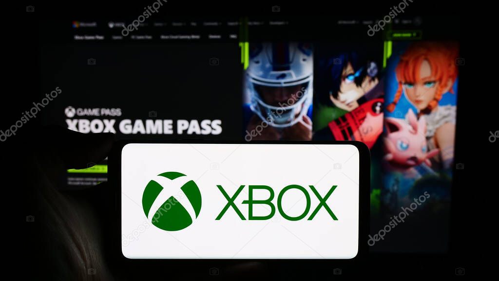 Stuttgart, Germany - 02-14-2024: Person holding cellphone with logo of video game console Xbox (Microsoft) in front of business webpage. Focus on phone display.