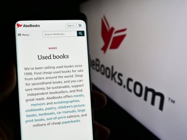 Stuttgart, Almanya - 02-19-2024: Kanada e-ticaret şirketi AbeBooks Inc. 'in internet sayfası ile iş logosu önünde cep telefonu tutan kişi. Telefon ekranının merkezine odaklan.