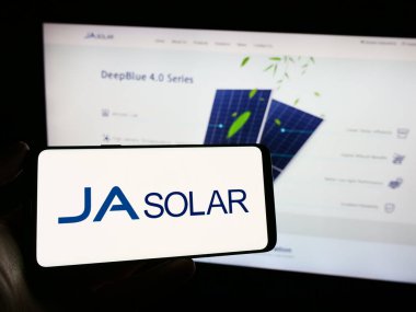 Stuttgart, Almanya - 02-19-2024: Çinli şirket JA Solar Holding Co. Ltd. 'nin logosunun bulunduğu cep telefonu sahibi kişi iş sayfasının önünde. Telefon ekranına odaklan.