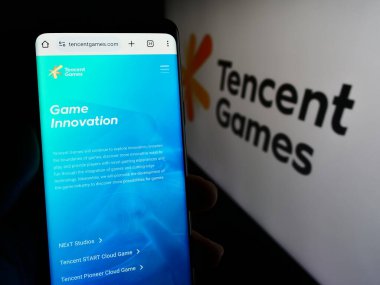 Stuttgart, Almanya - 02-22-2024: Çinli video oyunu şirketi Tencent Games 'in internet sayfası ile iş logosu önünde cep telefonu tutan kişi. Telefon ekranının merkezine odaklan.