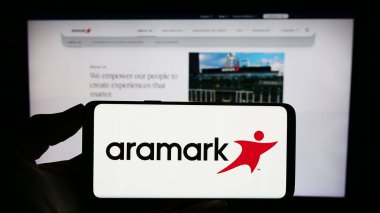 Stuttgart, Almanya - 02-22-2024: ABD gıda hizmetleri ve tesis yönetimi şirketi Aramark 'ın logosunun yer aldığı cep telefonu sahibi kişi web sayfasının önünde. Telefon ekranına odaklan.