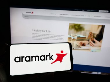 Stuttgart, Almanya - 02-22-2024: İnternet sayfası önünde Amerikan gıda hizmetleri ve tesis yönetimi şirketi Aramark 'ın logosunun bulunduğu cep telefonu sahibi kişi. Telefon ekranına odaklan.