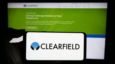 Stuttgart, Almanya - 02-22-2024: İnternet sayfasının önünde Amerikan bağlantı ürünleri şirketi Clearfield Inc. 'in logosu olan cep telefonu sahibi kişi. Telefon ekranına odaklan.