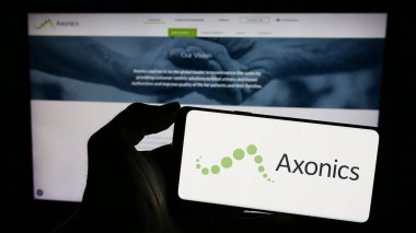 Stuttgart, Almanya - 02-22-2024: ABD modülasyon teknoloji şirketi Axonics Inc. 'in logosuna sahip cep telefonu sahibi kişi iş sayfasının önünde. Telefon ekranına odaklan.