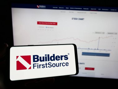 Stuttgart, Almanya - 02-22-2024: İnternet sayfası önünde ABD 'li inşaat malzemeleri şirketi Builders First Source Inc.' in logosu olan cep telefonu sahibi kişi. Telefon ekranına odaklan.