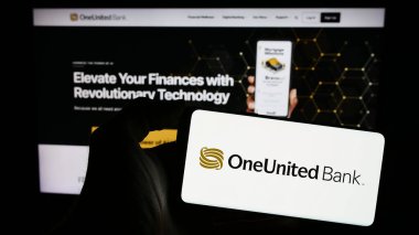 Stuttgart, Almanya - 02-22-2024: Amerikan finans hizmetleri şirketi OneUnited Bank 'ın logosuyla cep telefonu tutan kişi web sayfasının önünde. Telefon ekranına odaklan.