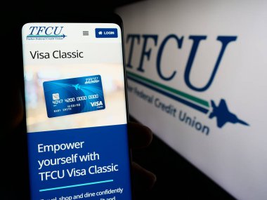 Stuttgart, Germany - 02-22-2024: Person holding cellphone with webpage of US financial company Tinker Federal Credit Union (TFCU) with logo. Focus on center of phone display. clipart