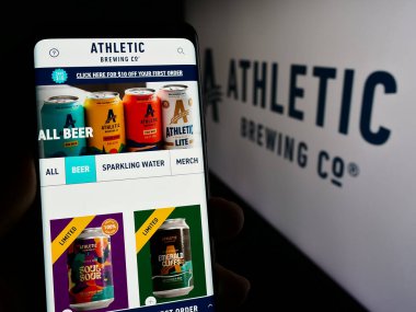 Stuttgart, Almanya - 02-22-2024: ABD 'li içecek şirketi Athletic Brewing Company' nin web sayfası ile logo önünde akıllı telefon tutan kişi. Telefon ekranının merkezine odaklan.