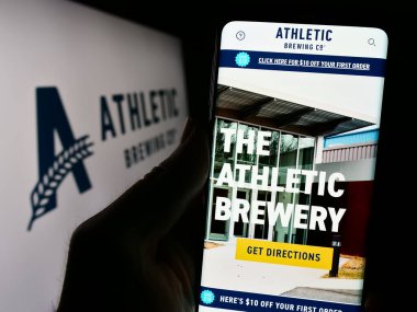 Stuttgart, Almanya - 02-22-2024: ABD 'li içecek şirketi Athletic Brewing Company' nin logo önündeki web sayfası ile cep telefonu tutan kişi. Telefon ekranının merkezine odaklan.